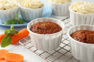 Photo of Delicious carrot muffins and fresh vegetables on white wooden table, closeup