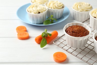 Photo of Delicious carrot muffins and fresh vegetables on white wooden table, closeup