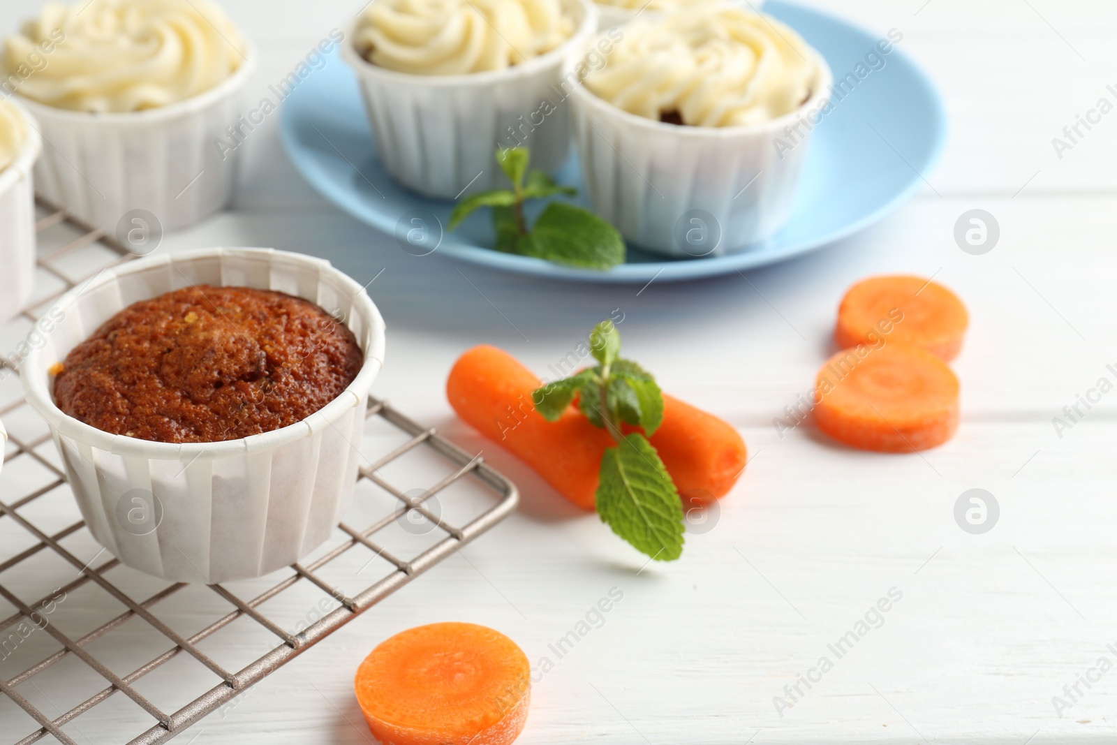 Photo of Delicious carrot muffins and fresh vegetables on white wooden table, closeup