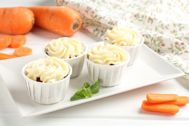 Photo of Delicious carrot muffins and fresh vegetables on white wooden table, closeup