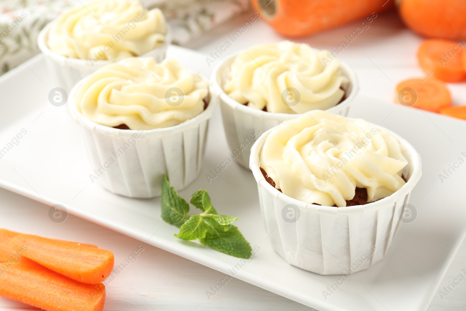 Photo of Delicious carrot muffins and fresh vegetables on white wooden table, closeup