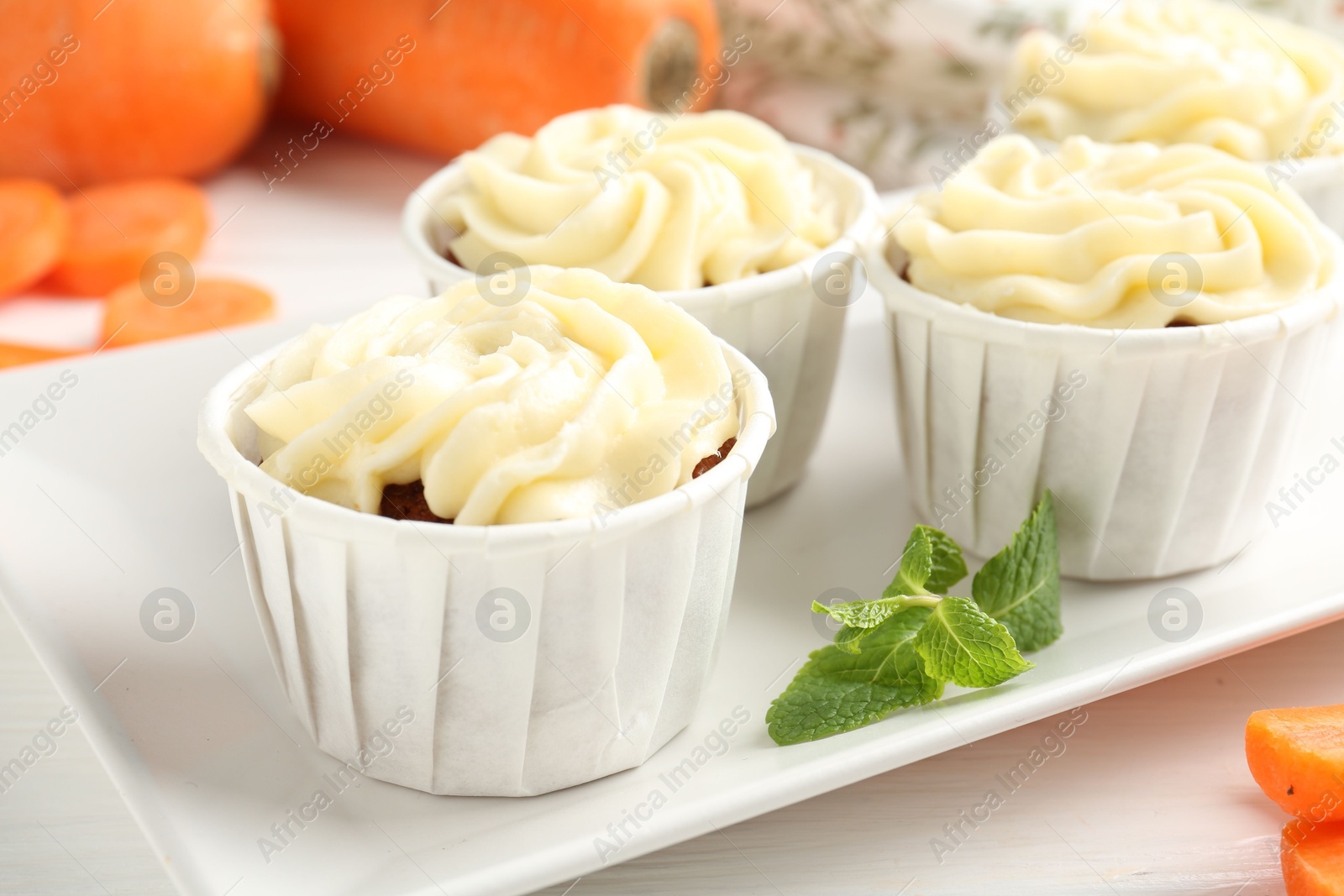 Photo of Delicious carrot muffins and fresh vegetable on white wooden table, closeup