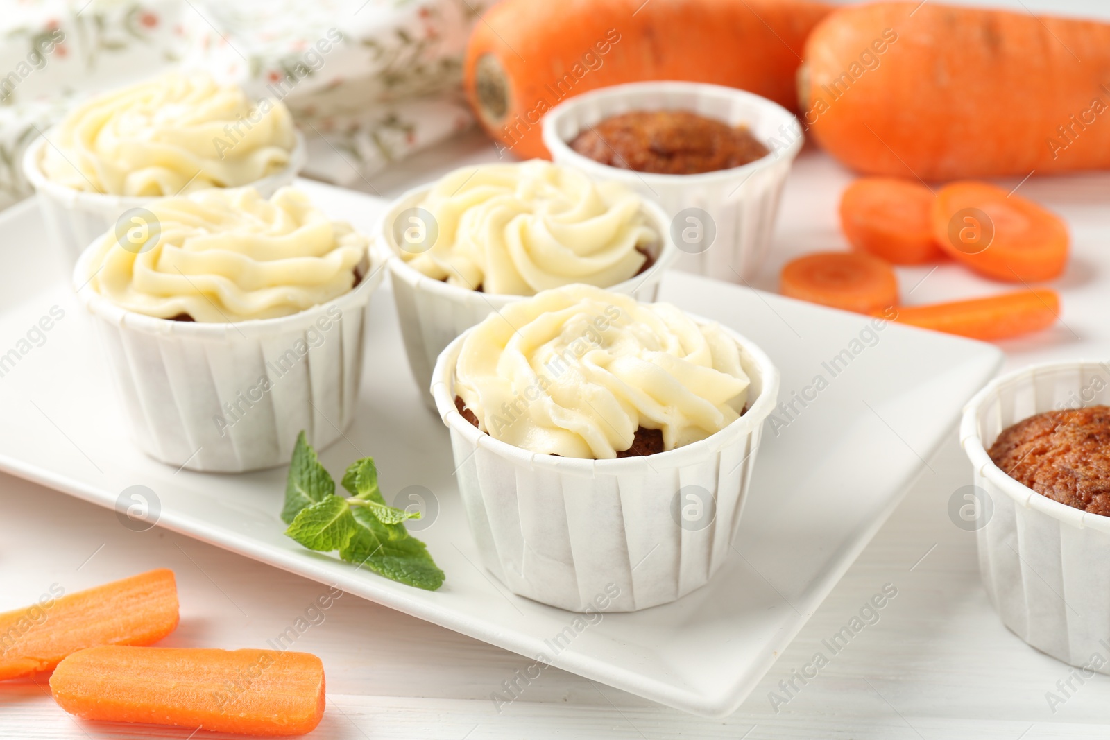 Photo of Delicious carrot muffins and fresh vegetables on white wooden table, closeup