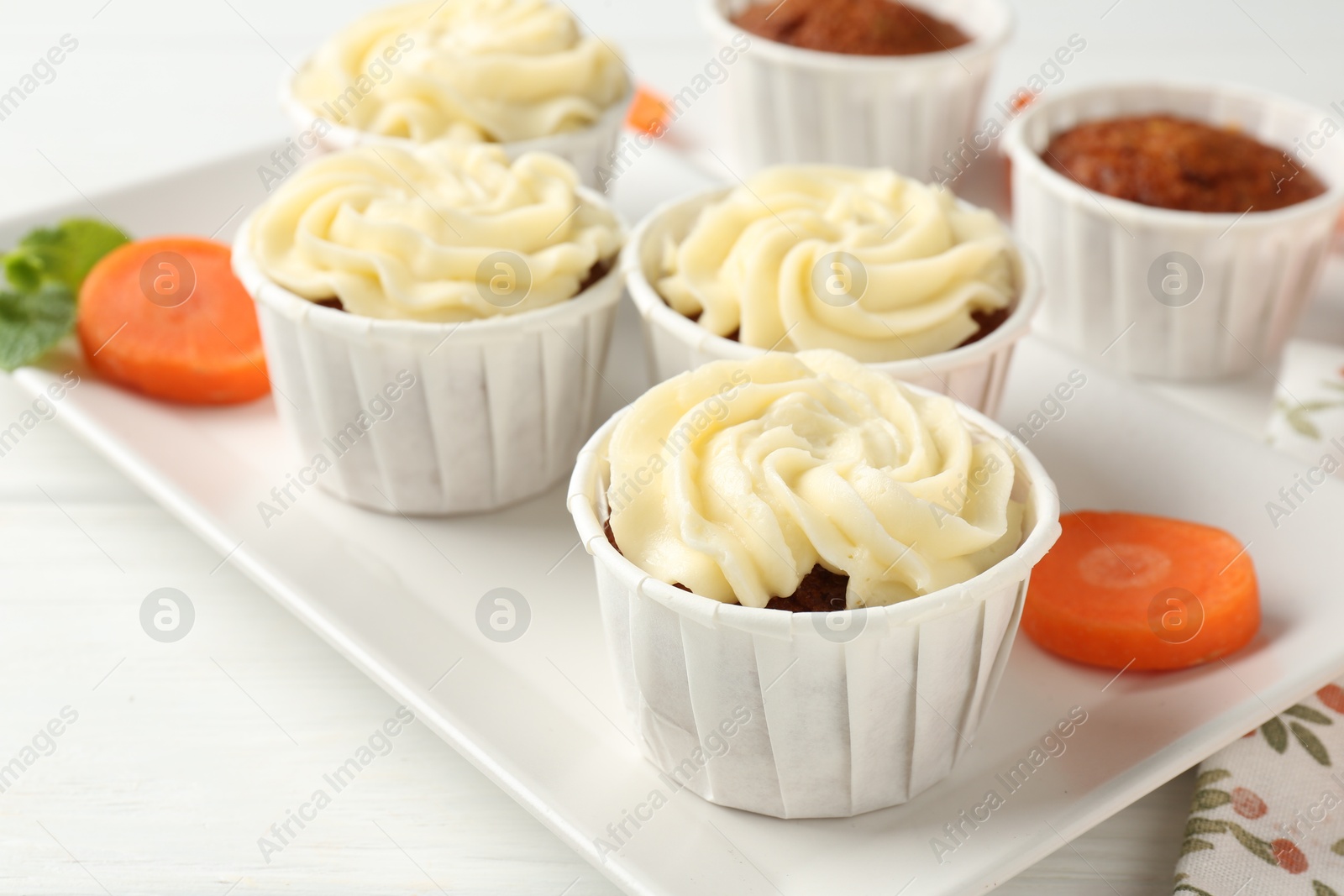 Photo of Delicious carrot muffins and fresh vegetable on white wooden table, closeup