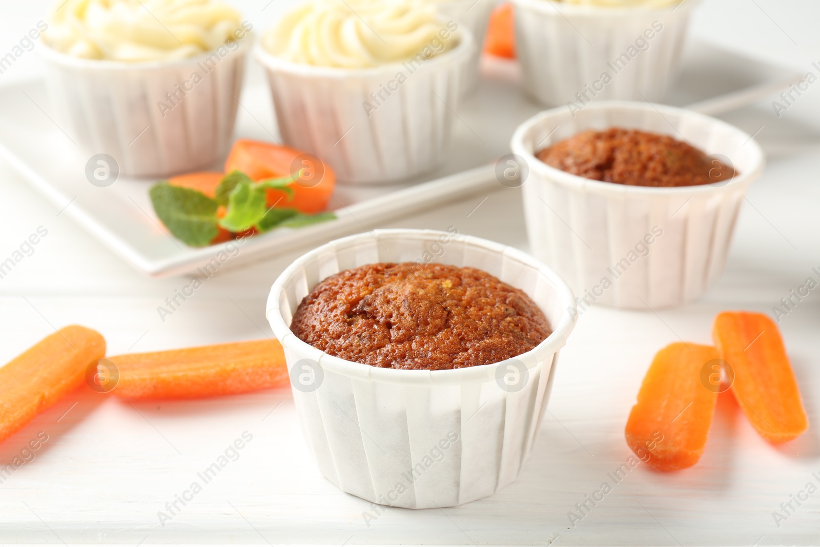 Photo of Delicious carrot muffins and fresh vegetables on white wooden table, closeup