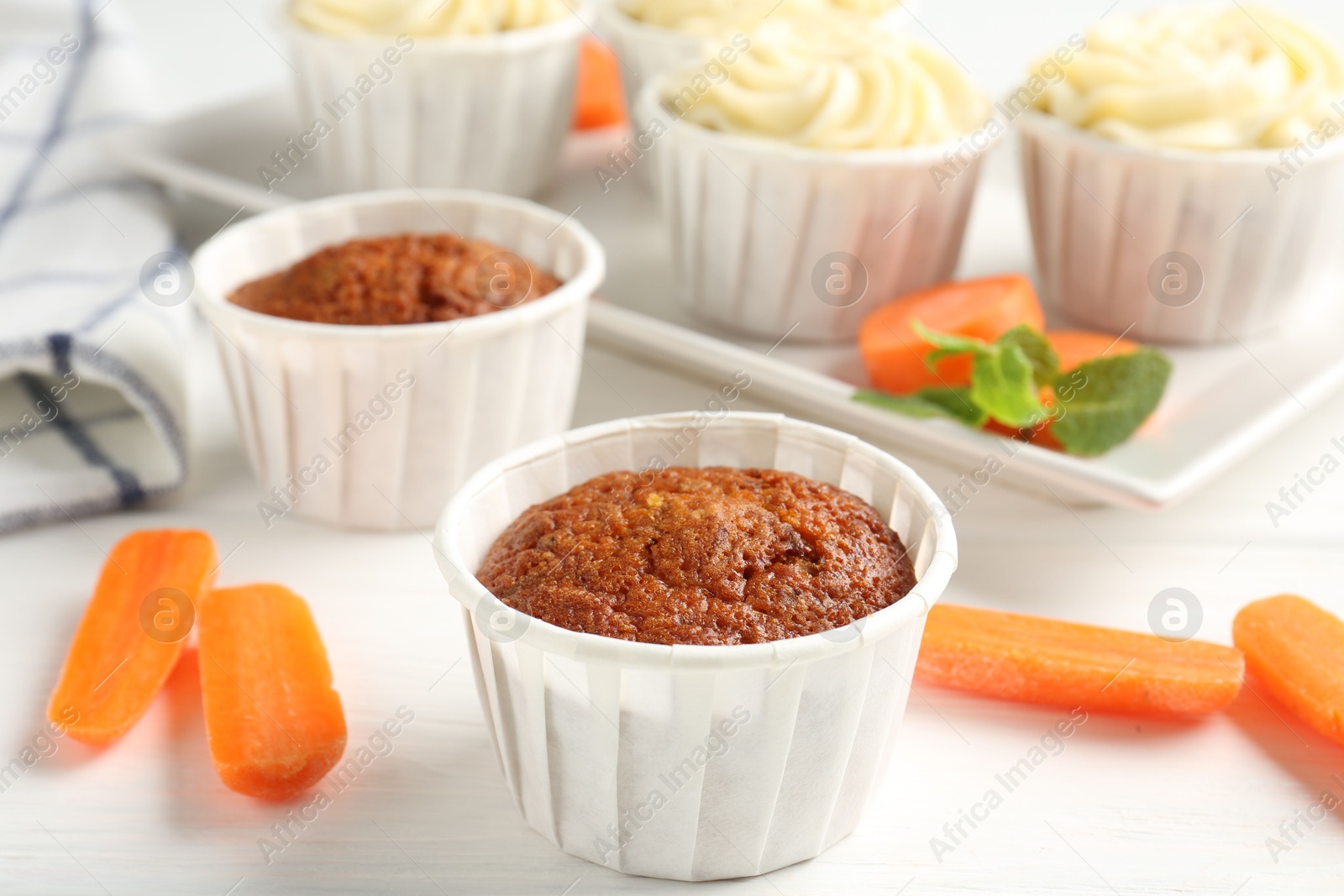 Photo of Delicious carrot muffins and fresh vegetables on white wooden table, closeup