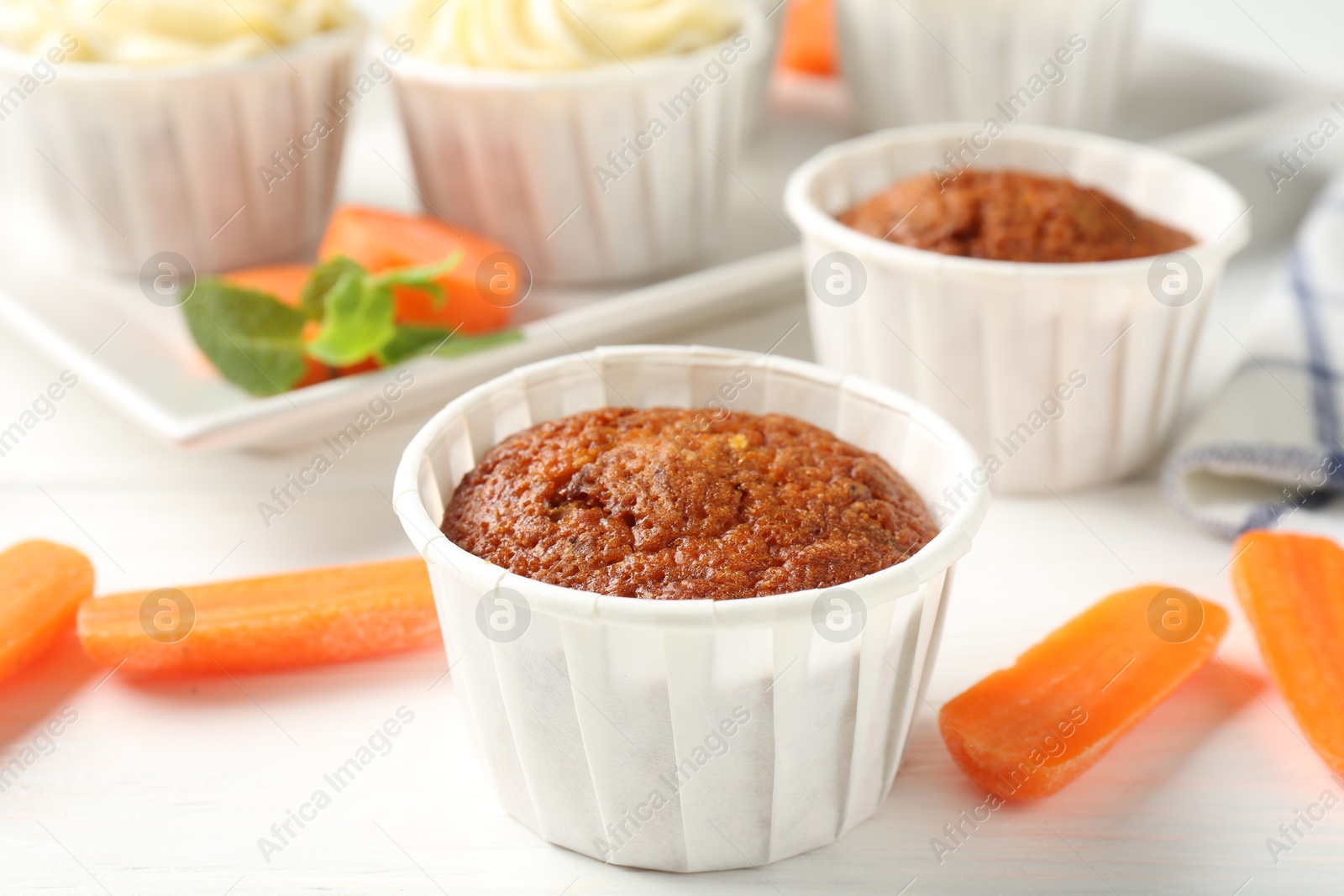 Photo of Delicious carrot muffins and fresh vegetables on white wooden table, closeup