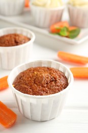 Photo of Delicious carrot muffins and fresh vegetables on white wooden table, closeup