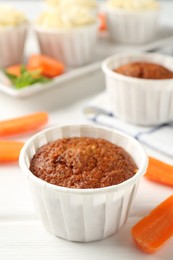 Photo of Delicious carrot muffins and fresh vegetables on white wooden table, closeup