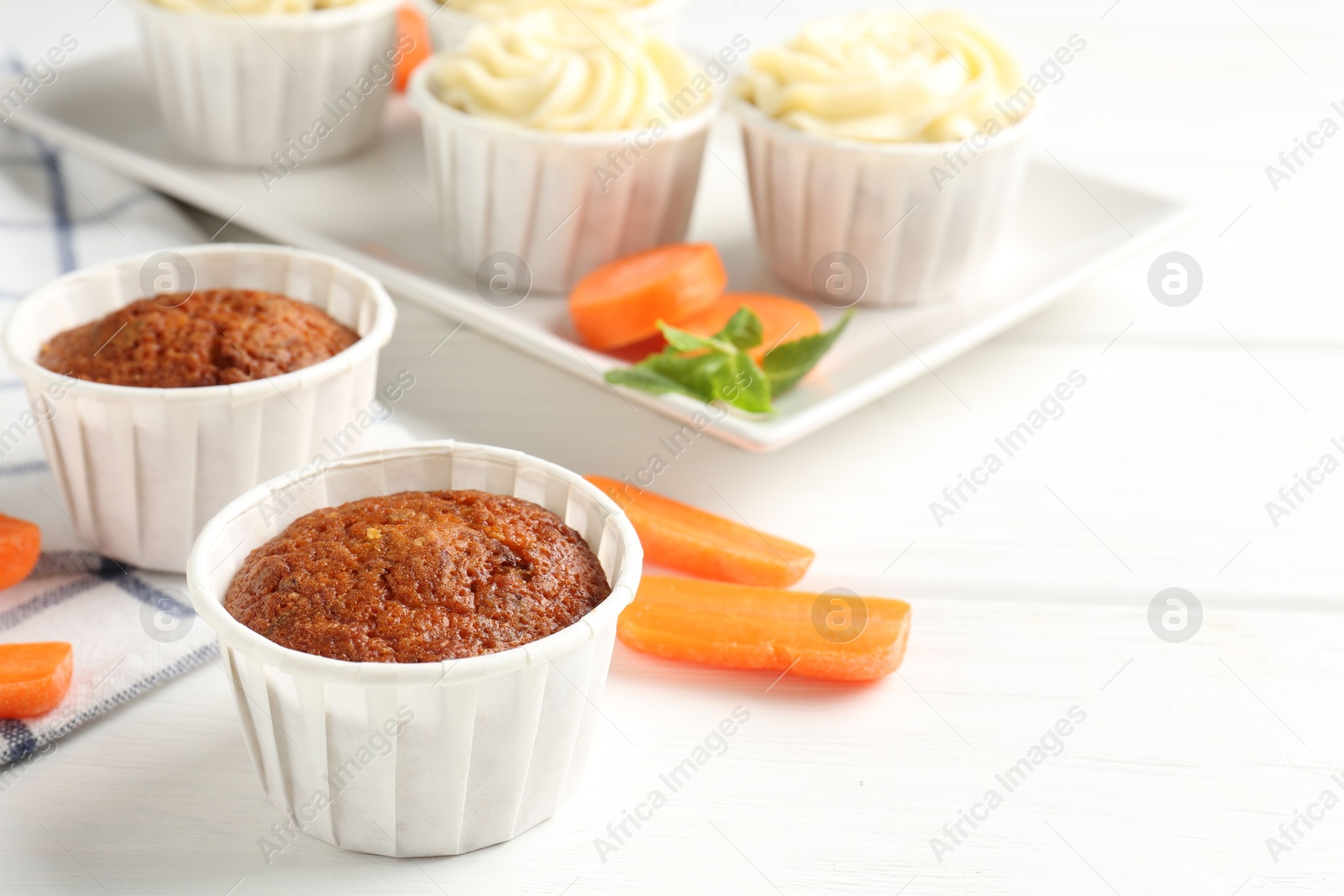 Photo of Tasty carrot muffins and fresh vegetables on white wooden table, closeup. Space for text