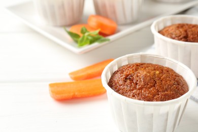 Photo of Tasty carrot muffins and fresh vegetables on white wooden table, closeup. Space for text