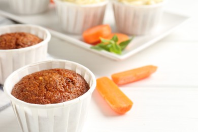 Photo of Tasty carrot muffins and fresh vegetables on white wooden table, closeup. Space for text