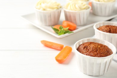 Photo of Tasty carrot muffins and fresh vegetables on white wooden table, closeup. Space for text