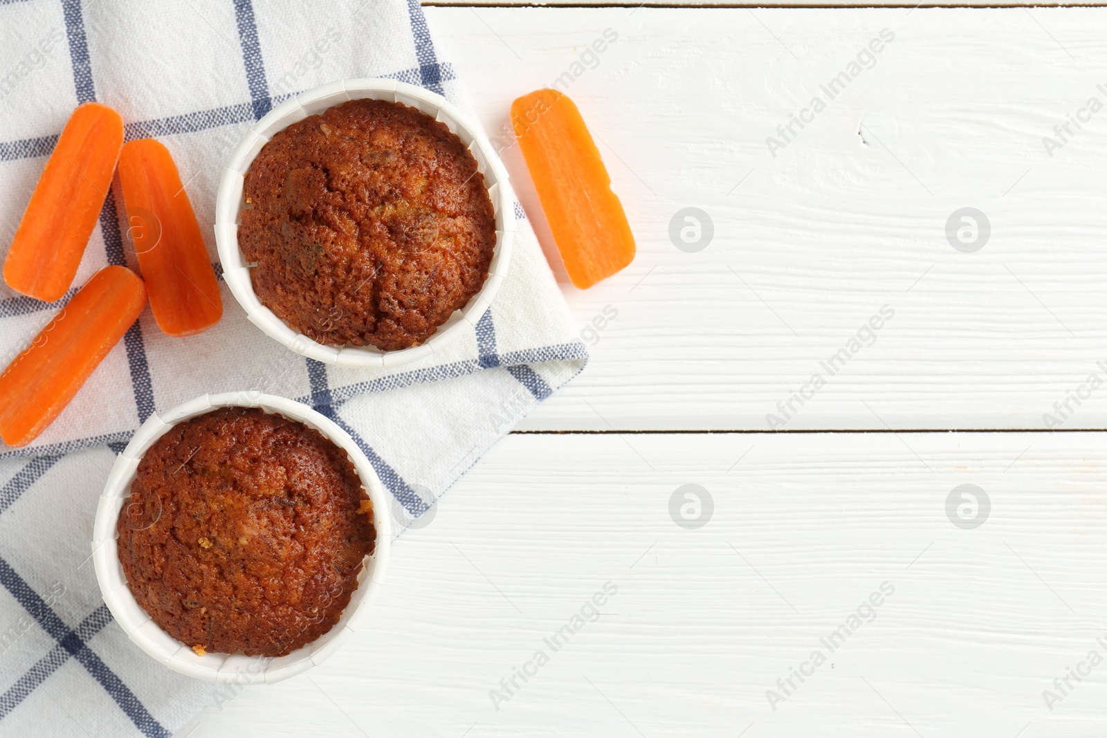 Photo of Tasty carrot muffins with fresh vegetables on white wooden table, flat lay. Space for text