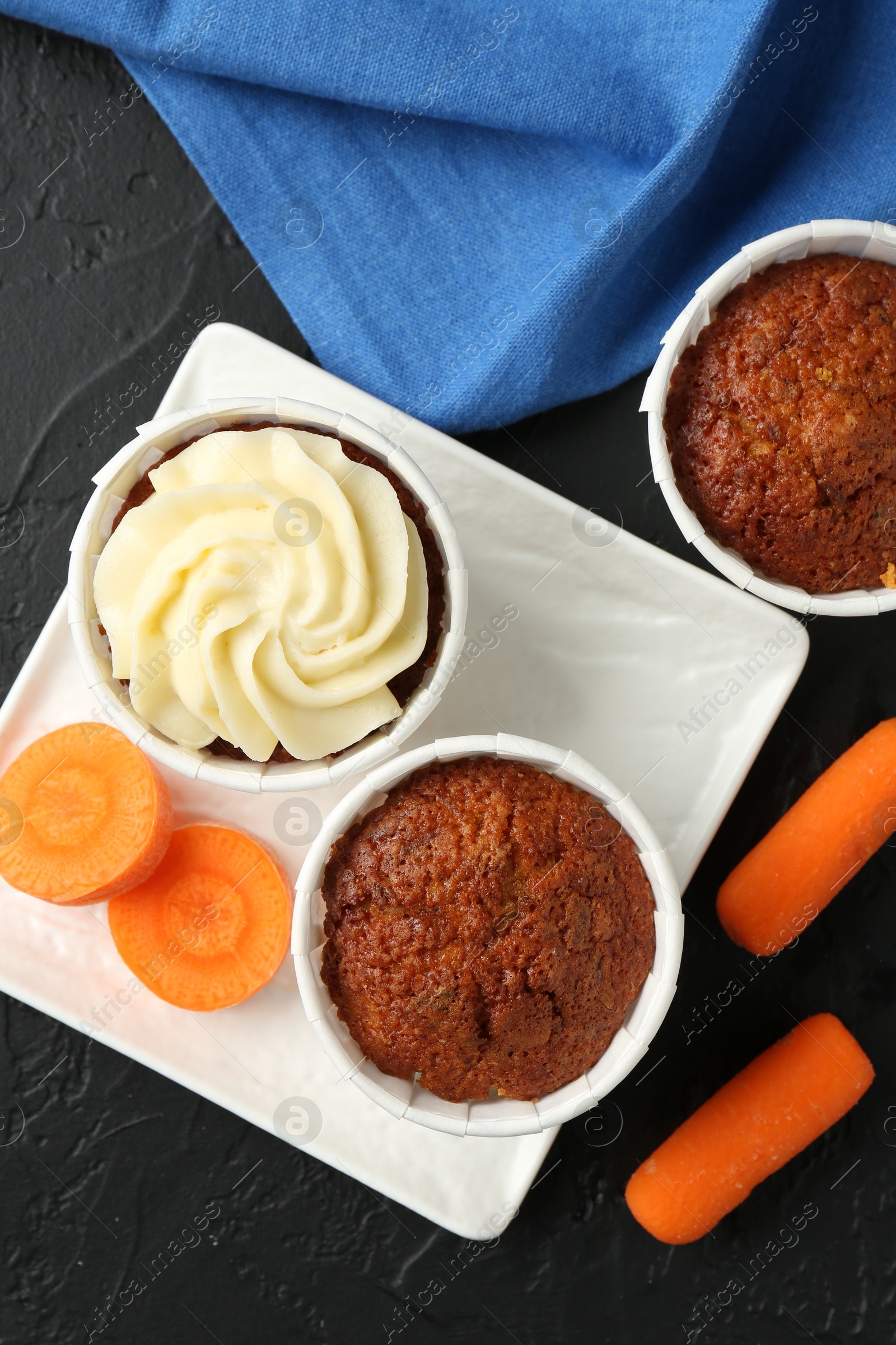 Photo of Tasty carrot muffins with fresh vegetables on grey table, flat lay