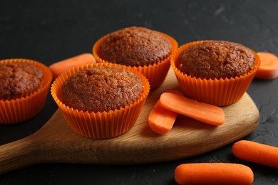 Photo of Delicious carrot muffins with fresh vegetables on black table, closeup