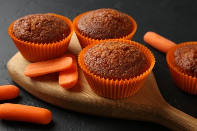 Photo of Delicious carrot muffins with fresh vegetables on black table, closeup