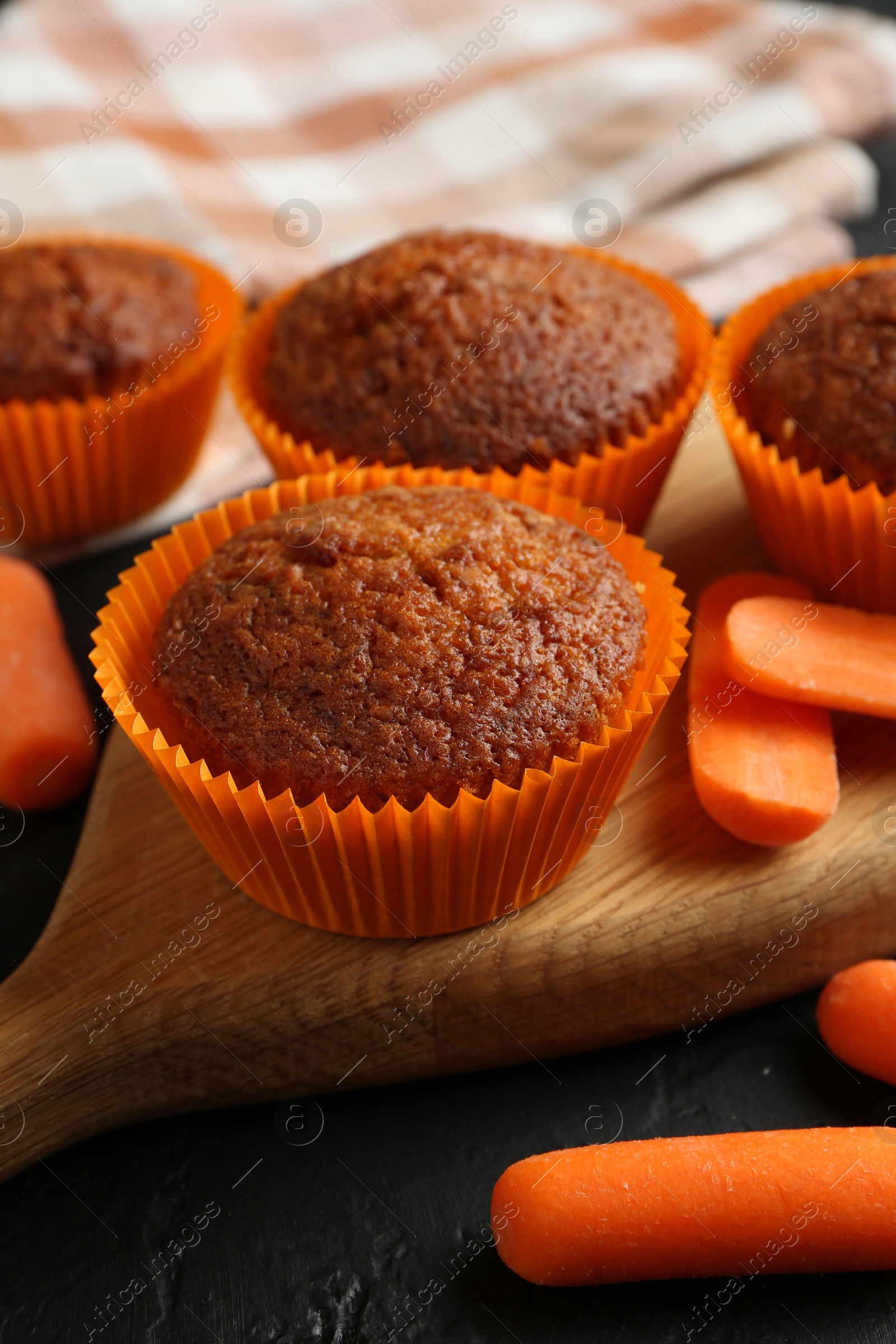 Photo of Delicious carrot muffins with fresh vegetables on black table, closeup