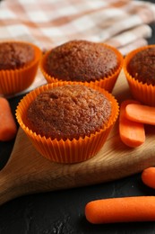 Photo of Delicious carrot muffins with fresh vegetables on black table, closeup