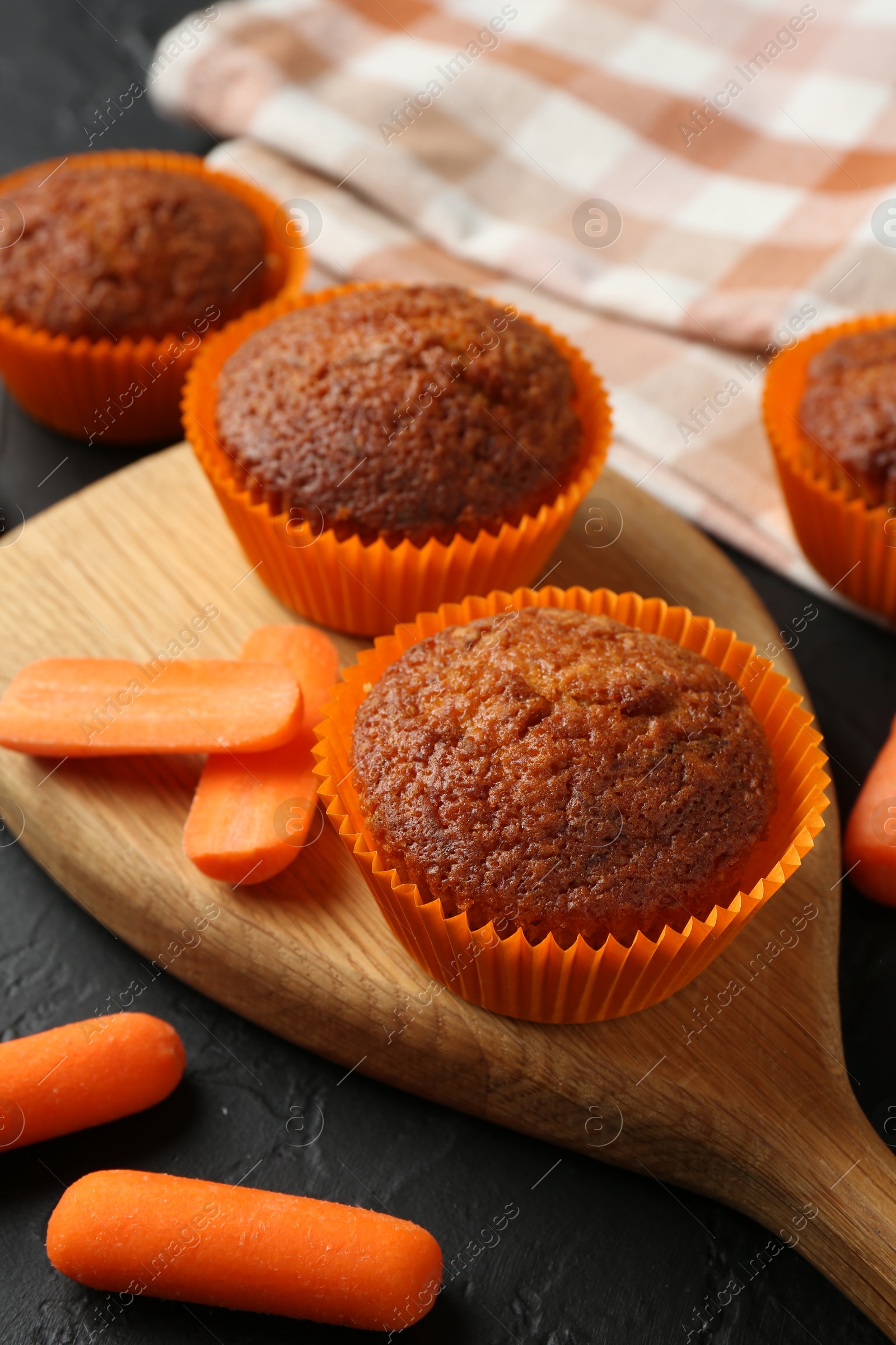 Photo of Delicious carrot muffins with fresh vegetables on black table, closeup