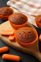 Photo of Delicious carrot muffins with fresh vegetables on black table, closeup