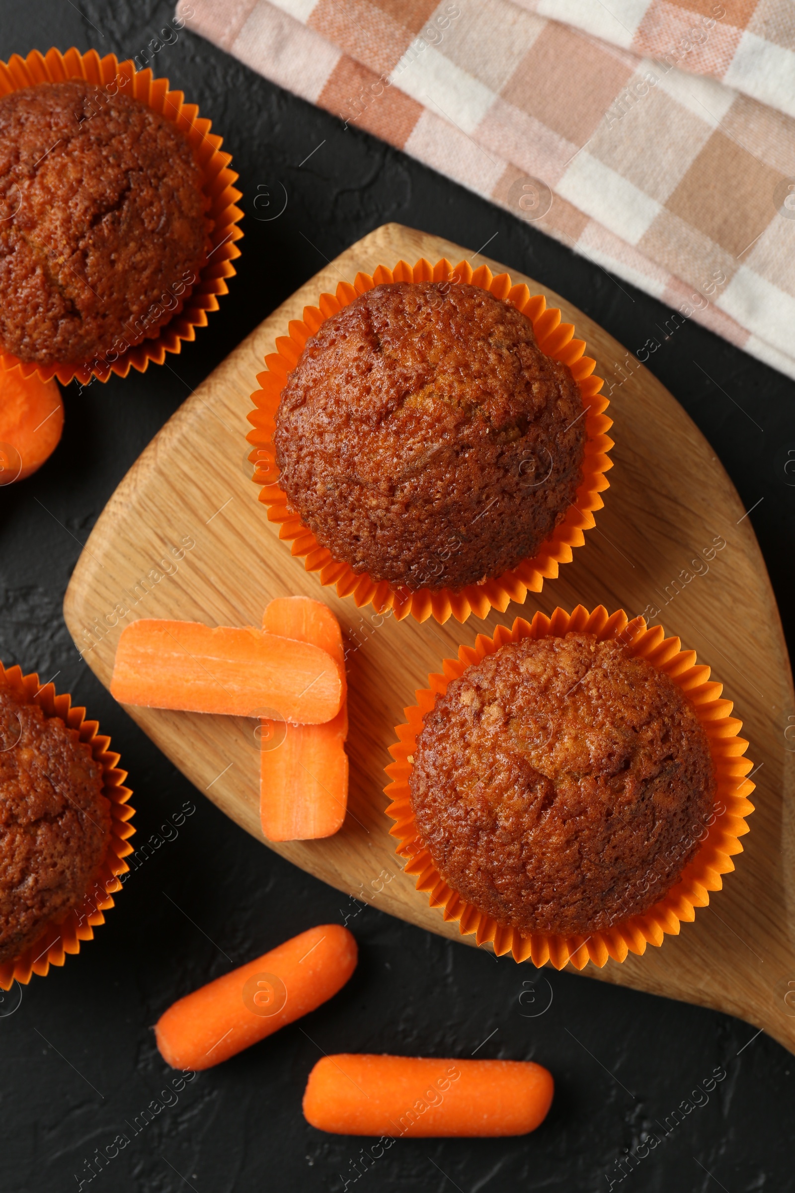 Photo of Tasty carrot muffins with fresh vegetables on black table, flat lay