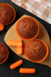 Photo of Tasty carrot muffins with fresh vegetables on black table, flat lay