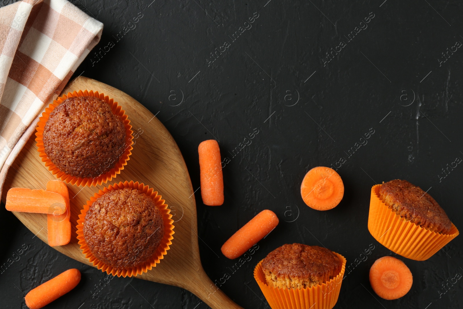 Photo of Delicious carrot muffins with fresh vegetables on black table, flat lay. Space for text