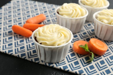 Photo of Delicious carrot muffins with fresh vegetables on black table, closeup