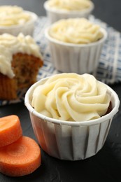 Photo of Tasty carrot muffins with fresh vegetable on black table, closeup