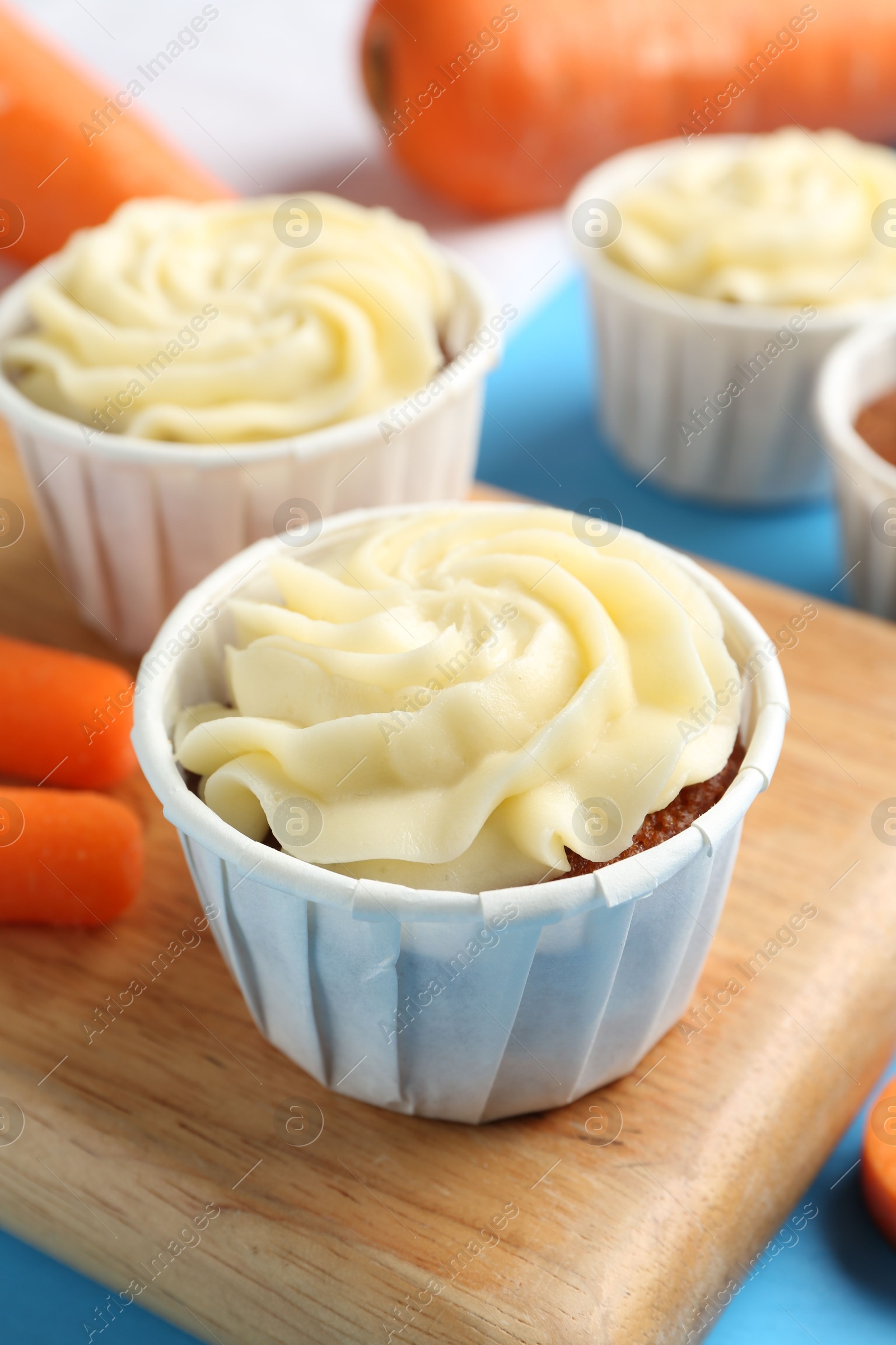 Photo of Tasty carrot muffins with fresh vegetables on light blue table, closeup