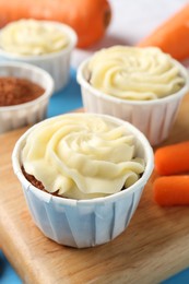 Photo of Tasty carrot muffins with fresh vegetables on light blue table, closeup