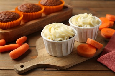 Photo of Tasty carrot muffins with fresh vegetables on wooden table, closeup