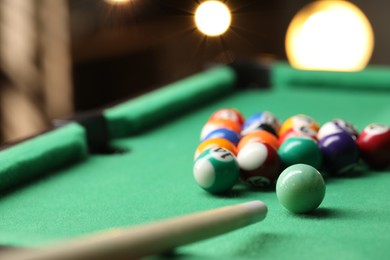 Photo of Billiard balls in triangle and cue on green table indoors, closeup. Space for text