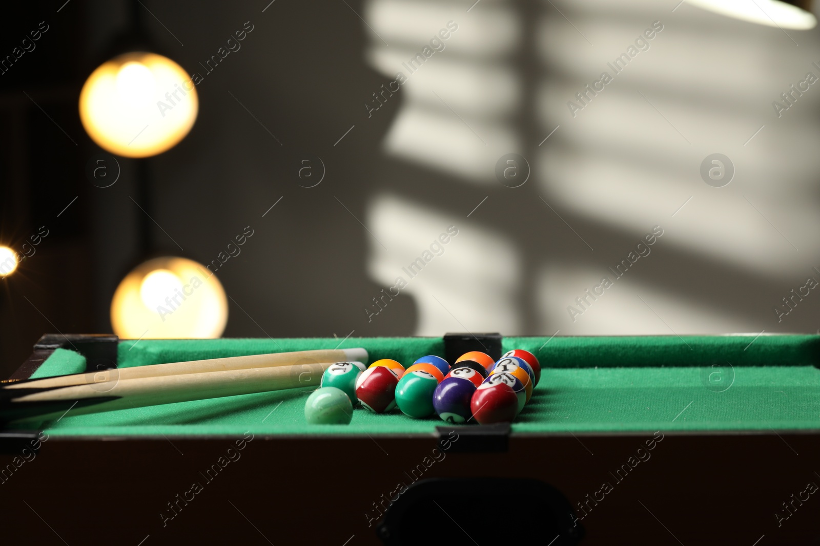 Photo of Billiard balls in triangle and cues on green table indoors. Space for text