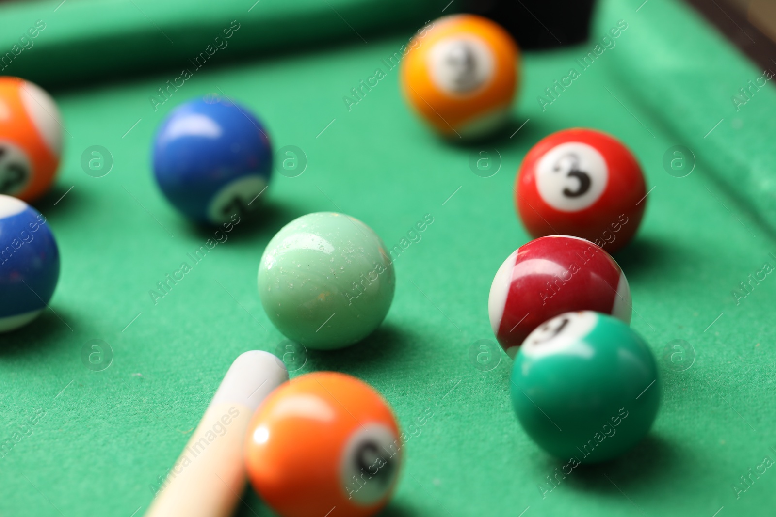 Photo of Many colorful billiard balls and cue on green table, closeup