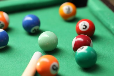 Photo of Many colorful billiard balls and cue on green table, closeup