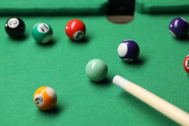 Photo of Many colorful billiard balls and cue on green table, closeup