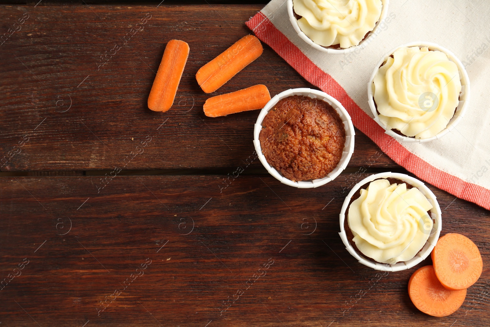 Photo of Delicious carrot muffins and fresh vegetables on wooden table, flat lay. Space for text