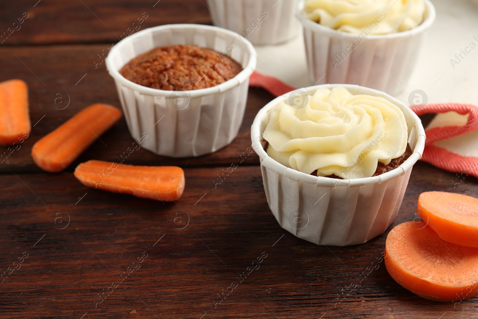 Photo of Delicious carrot muffins and fresh vegetables on wooden table, closeup