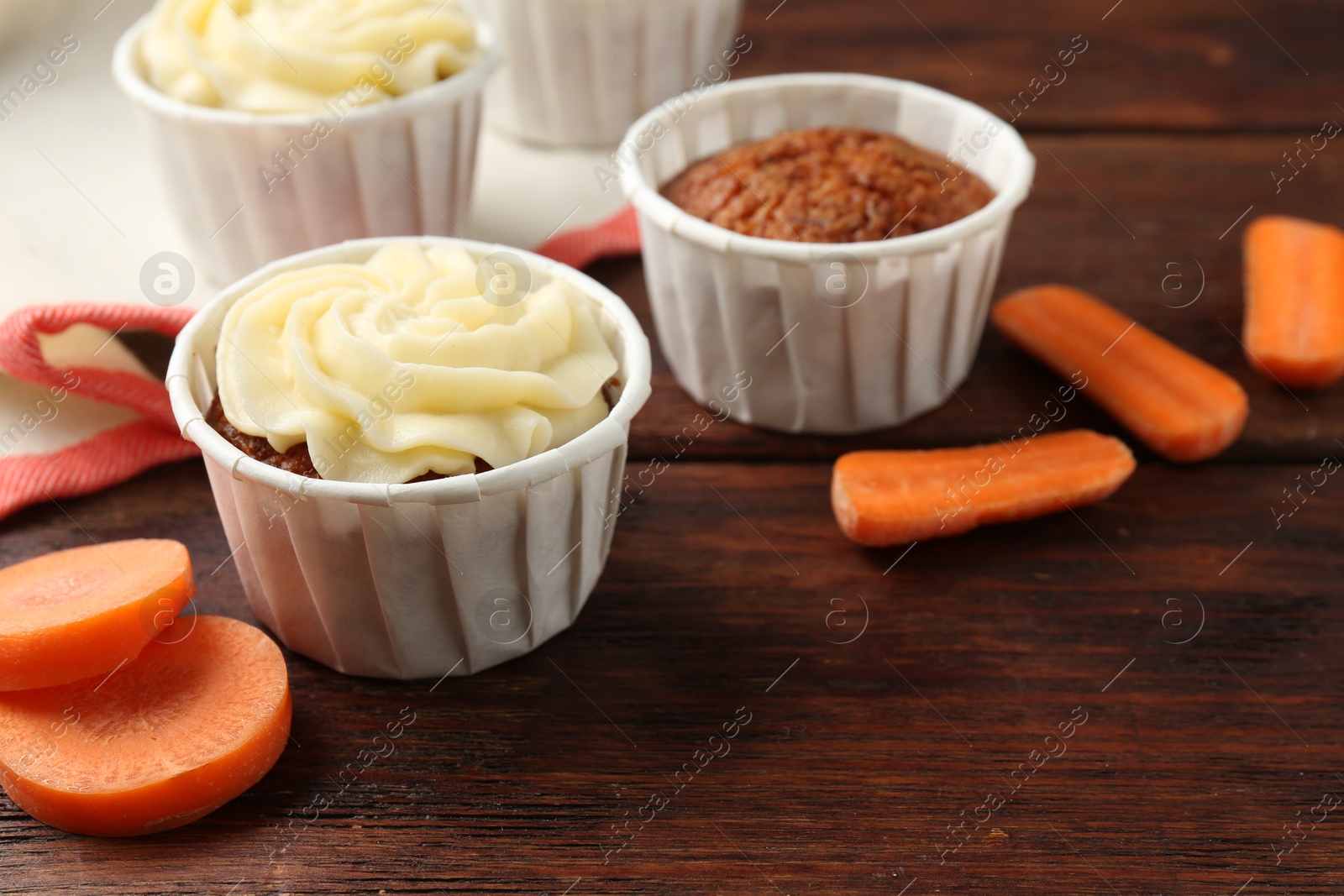 Photo of Delicious carrot muffins and fresh vegetables on wooden table, closeup