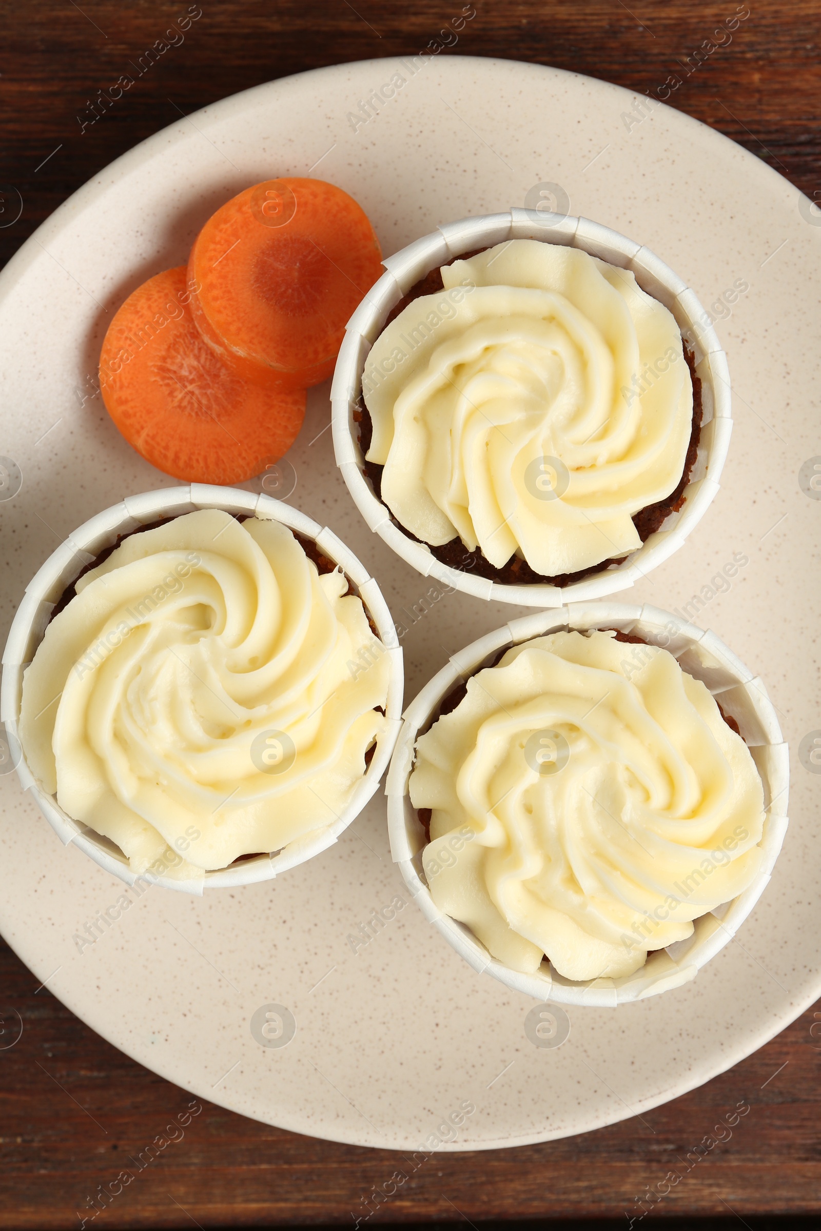 Photo of Delicious carrot muffins and fresh vegetable on wooden table, top view