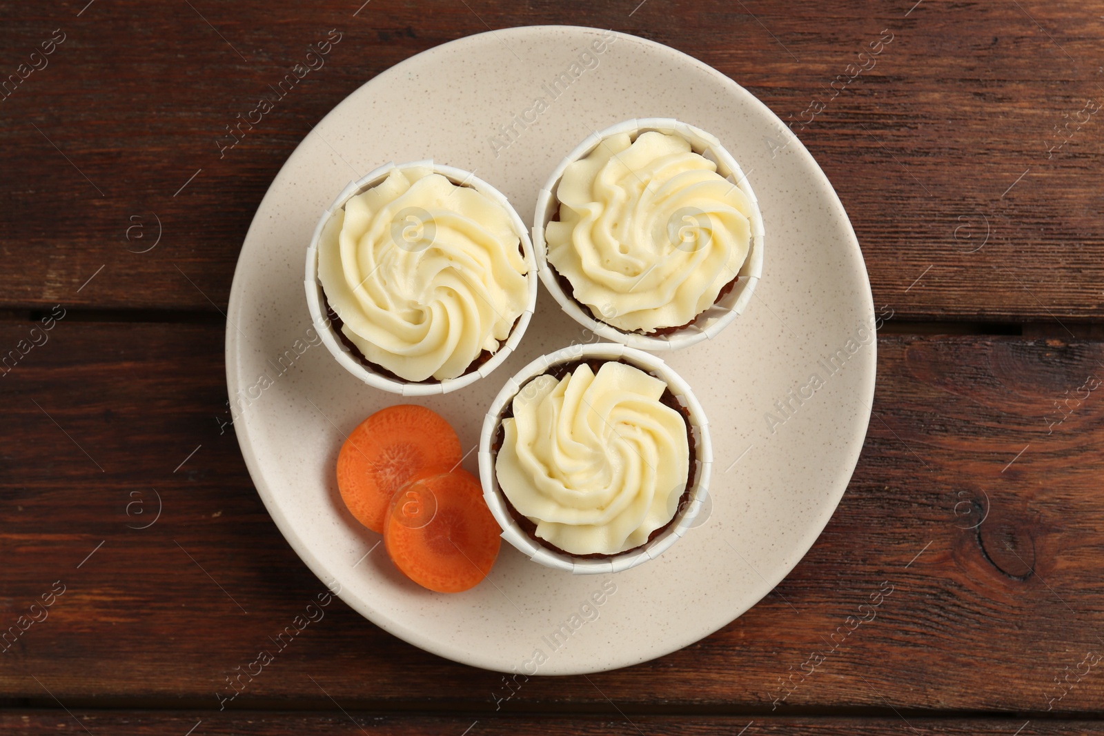 Photo of Delicious carrot muffins and fresh vegetable on wooden table, top view