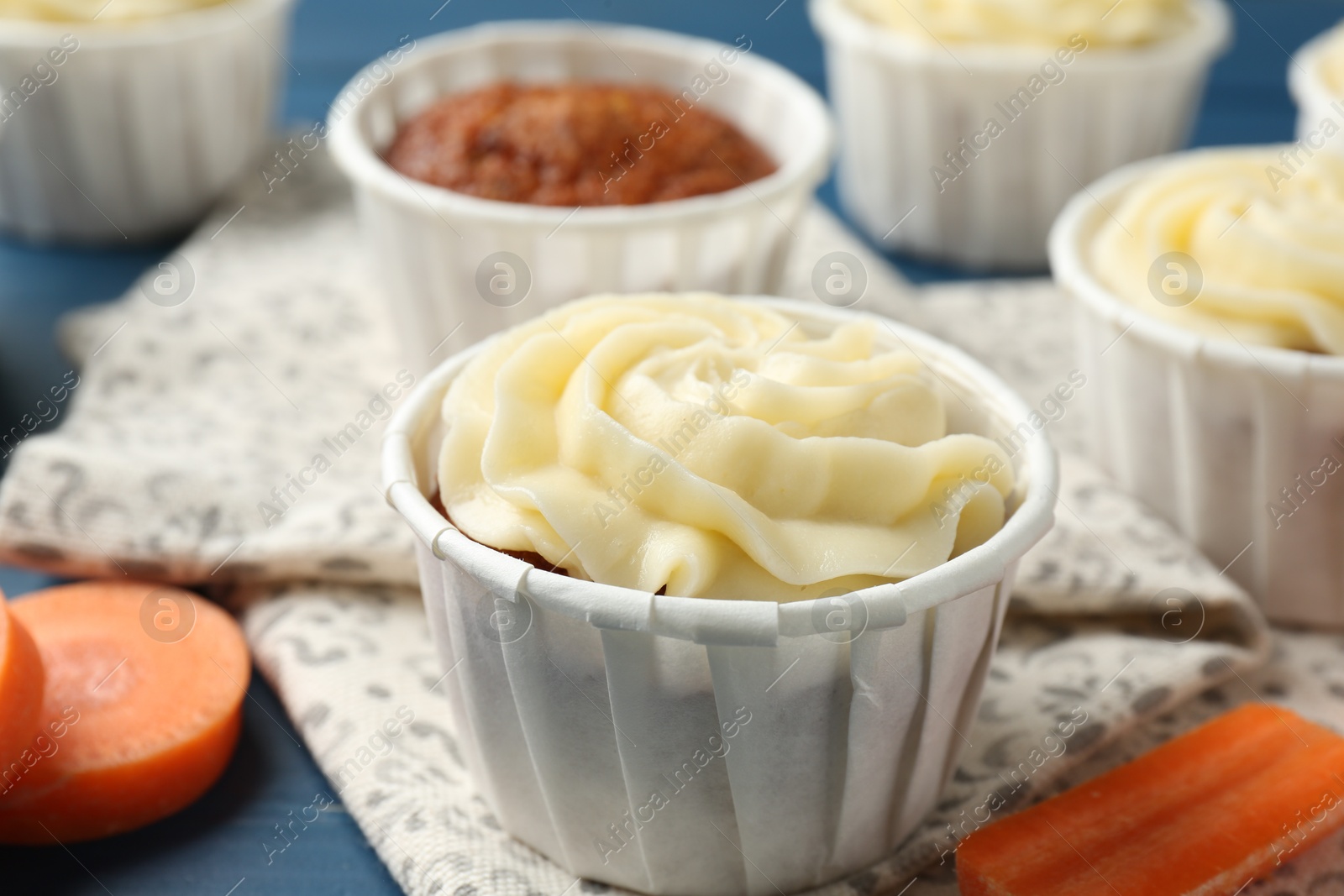 Photo of Delicious carrot muffins and fresh vegetables on blue table, closeup