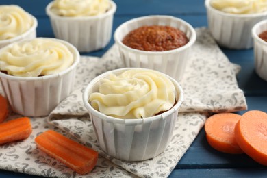 Photo of Delicious carrot muffins and fresh vegetables on blue wooden table, closeup