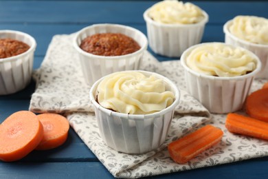 Photo of Delicious carrot muffins and fresh vegetables on blue wooden table, closeup