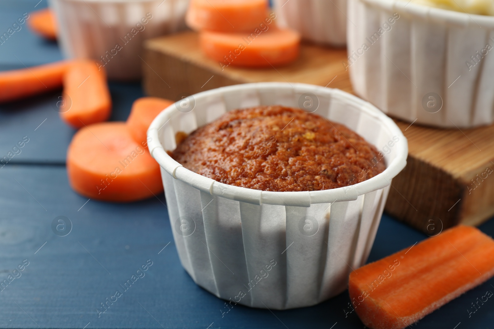 Photo of Delicious carrot muffins and fresh vegetables on blue wooden table, closeup