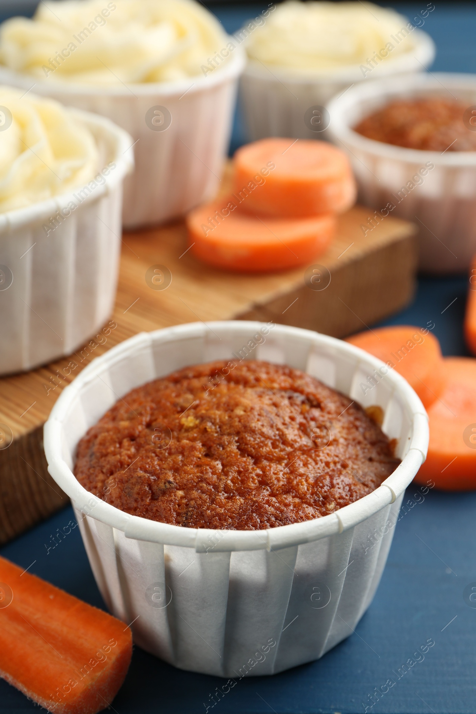 Photo of Delicious carrot muffins and fresh vegetables on blue table, closeup