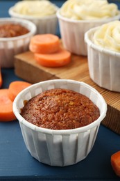 Photo of Delicious carrot muffins and fresh vegetables on blue wooden table, closeup