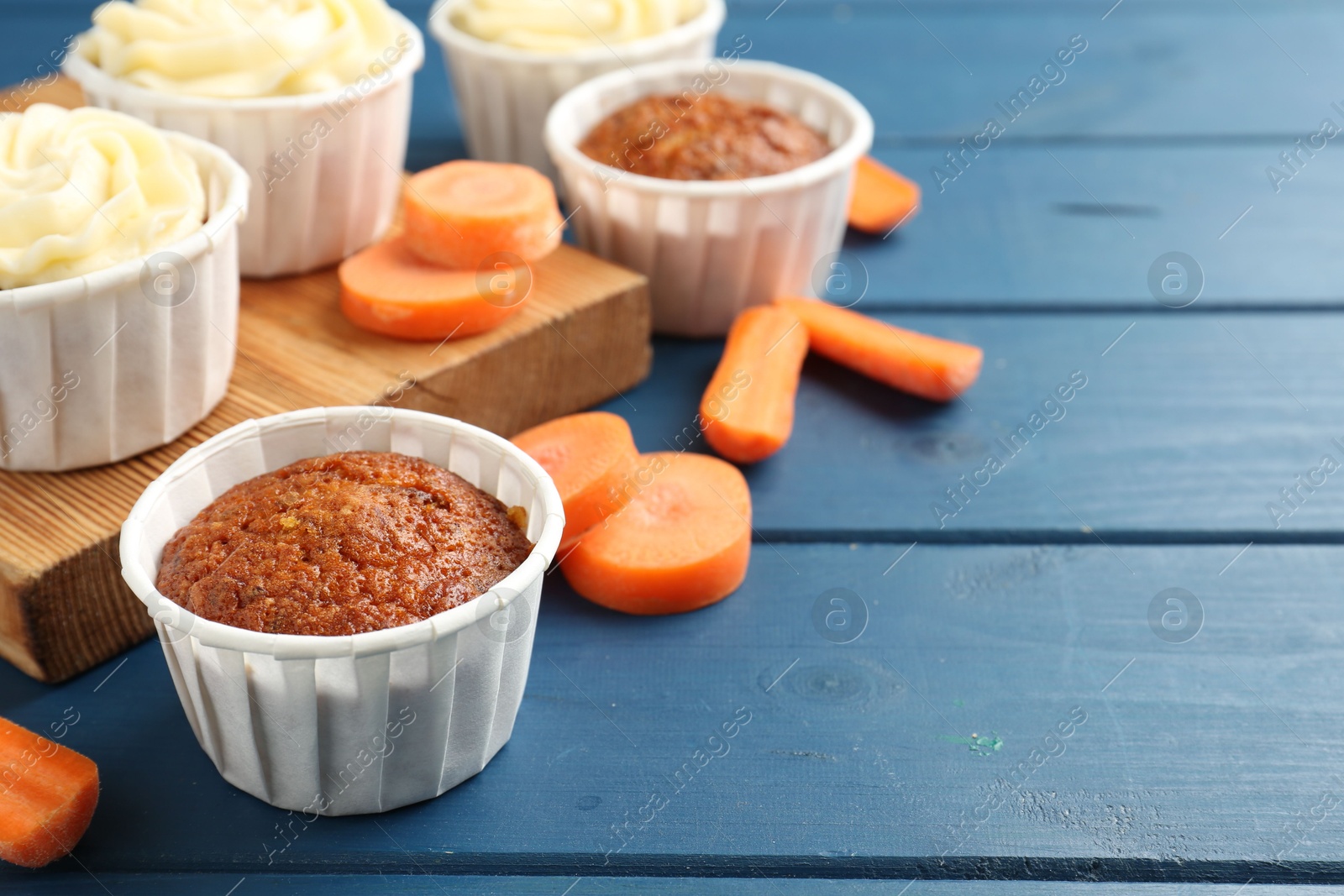 Photo of Delicious carrot muffins and fresh vegetables on blue wooden table, closeup. Space for text